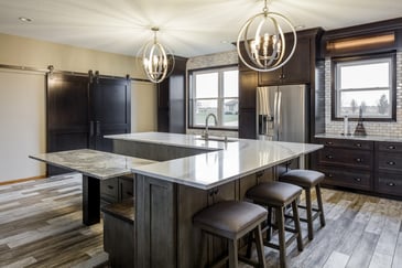 A kitchen with a marble countertop, oval pendant lights, and wooden floors