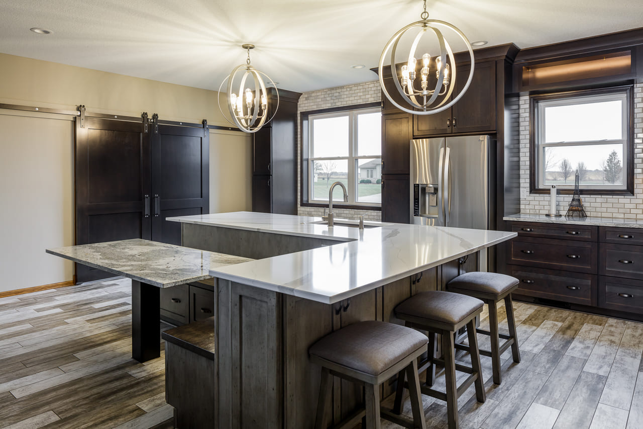 A kitchen with marble countertop, oval pendant lights and wooden floors